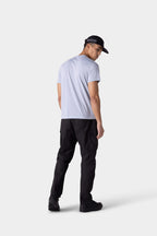 A man faces away, glancing over his shoulder. He wears the 686 Mens Everywhere drirelease® Tech Tee in light gray, with black pants, sneakers, and a cap against a plain light-colored background.