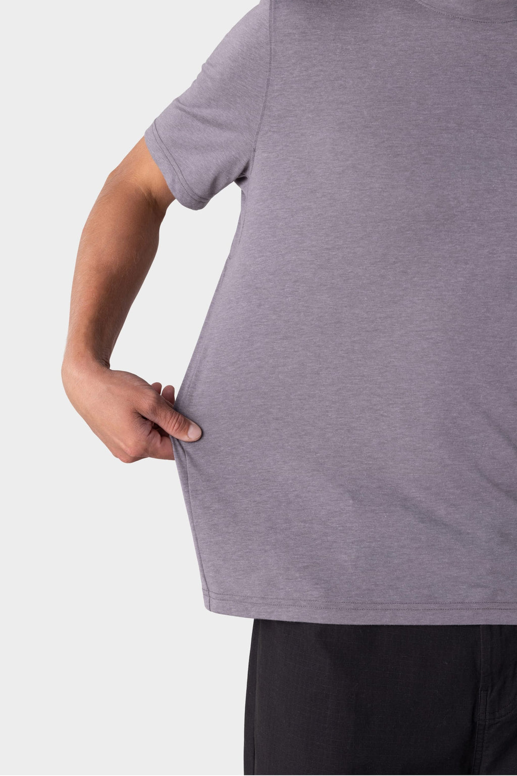 A person wearing the 686 Mens Everywhere drirelease® Tech Tee in grey pulls the side of the shirt outward with one hand, highlighting its stretch and fit. Only their upper body is visible; they also wear black pants.