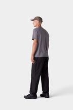Someone faces away wearing the 686 Mens Everywhere drirelease® Tech Tee in gray, paired with black pants, black sneakers, and a gray cap. The background is plain and light-colored.