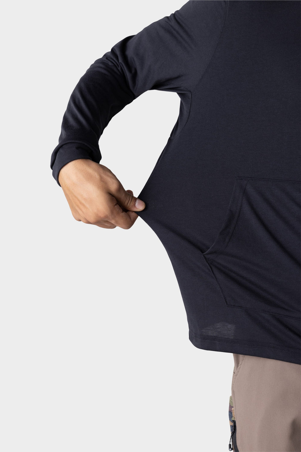 A person stretches the side of a 686 Mens Everywhere drirelease® Long Sleeve Hooded Tech Tee, highlighting its flexibility. Only the torso, arm, and part of the pants are visible against a plain light background.