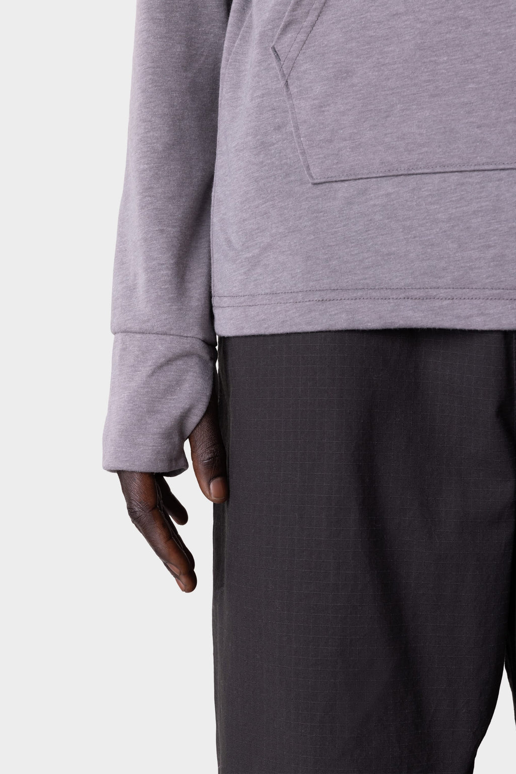 A close-up of a person wearing the 686 Mens Everywhere drirelease® Long Sleeve Hooded Tech Tee by 686, paired with dark pants, their left arm relaxed at their side against a plain light background.