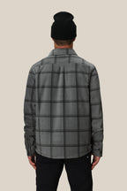 A person is shown from the back wearing the 686 Mens Sierra Fleece Flannel in black, standing against a plain light beige background—a perfect layering piece for spring riding.
