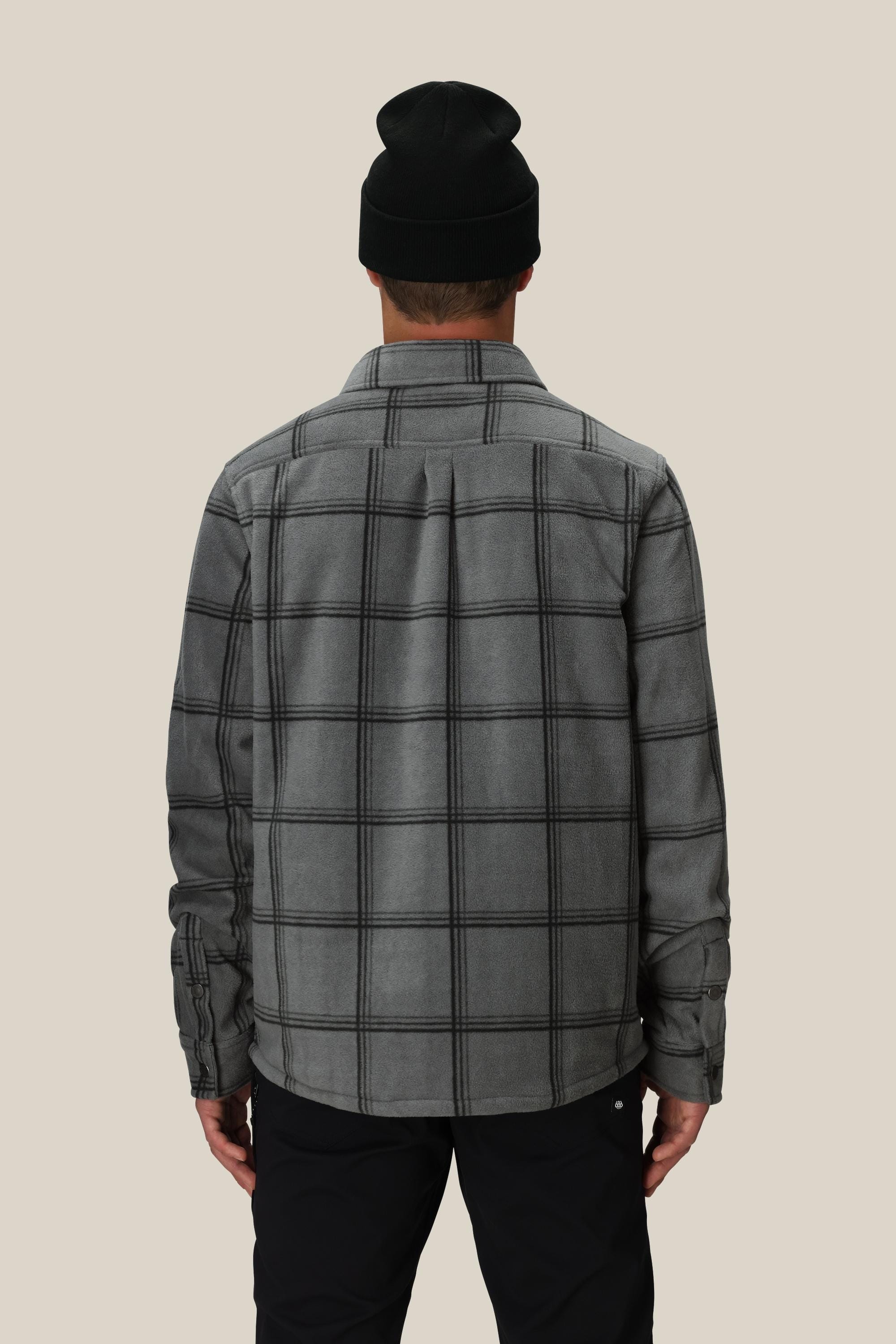 A person is shown from the back wearing the 686 Mens Sierra Fleece Flannel in black, standing against a plain light beige background—a perfect layering piece for spring riding.
