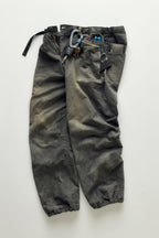 The 686 Cruiser Pant - Wide Fit by 686 in dark gray is shown laid flat on a light surface, featuring a bungee hem and belt, with a carabiner with keys, multitool, flashlight, and smartphone attached or in the pockets.