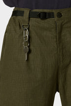 A close-up shows a person wearing the 686 Cruiser Pant - Wide Fit by 686 in olive green ripstop, styled with a black belt and silver keychain on the belt loop, paired with a dark shirt for a modern look.