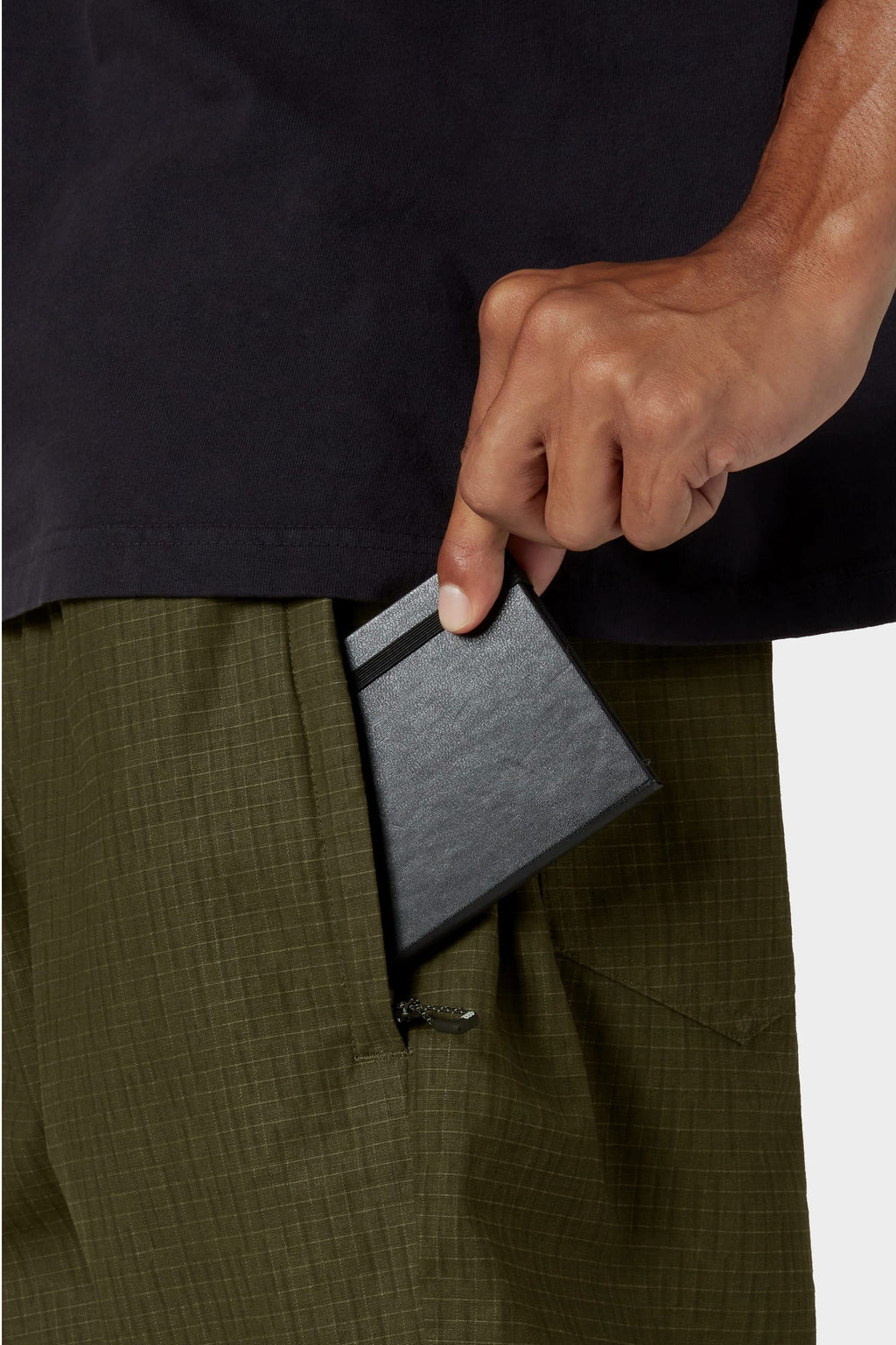 Someone wearing 686 Cruiser Pant - Wide Fit in olive green and a dark shirt puts a slim black wallet into the pant’s side pocket.
