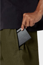 Someone wearing 686 Cruiser Pant - Wide Fit in olive green and a dark shirt puts a slim black wallet into the pant’s side pocket.