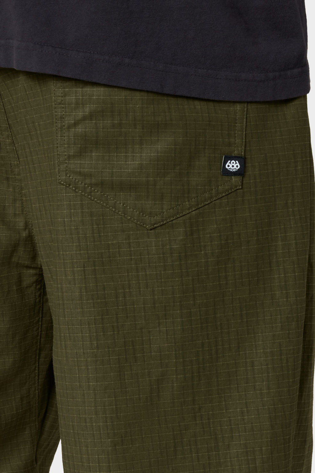 Close-up of a person wearing the 686 Cruiser Pant - Wide Fit in olive green ripstop fabric, featuring a visible back pocket with a small black tag, paired with a dark shirt.
