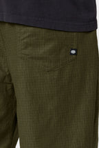 Close-up of a person wearing the 686 Cruiser Pant - Wide Fit in olive green ripstop fabric, featuring a visible back pocket with a small black tag, paired with a dark shirt.