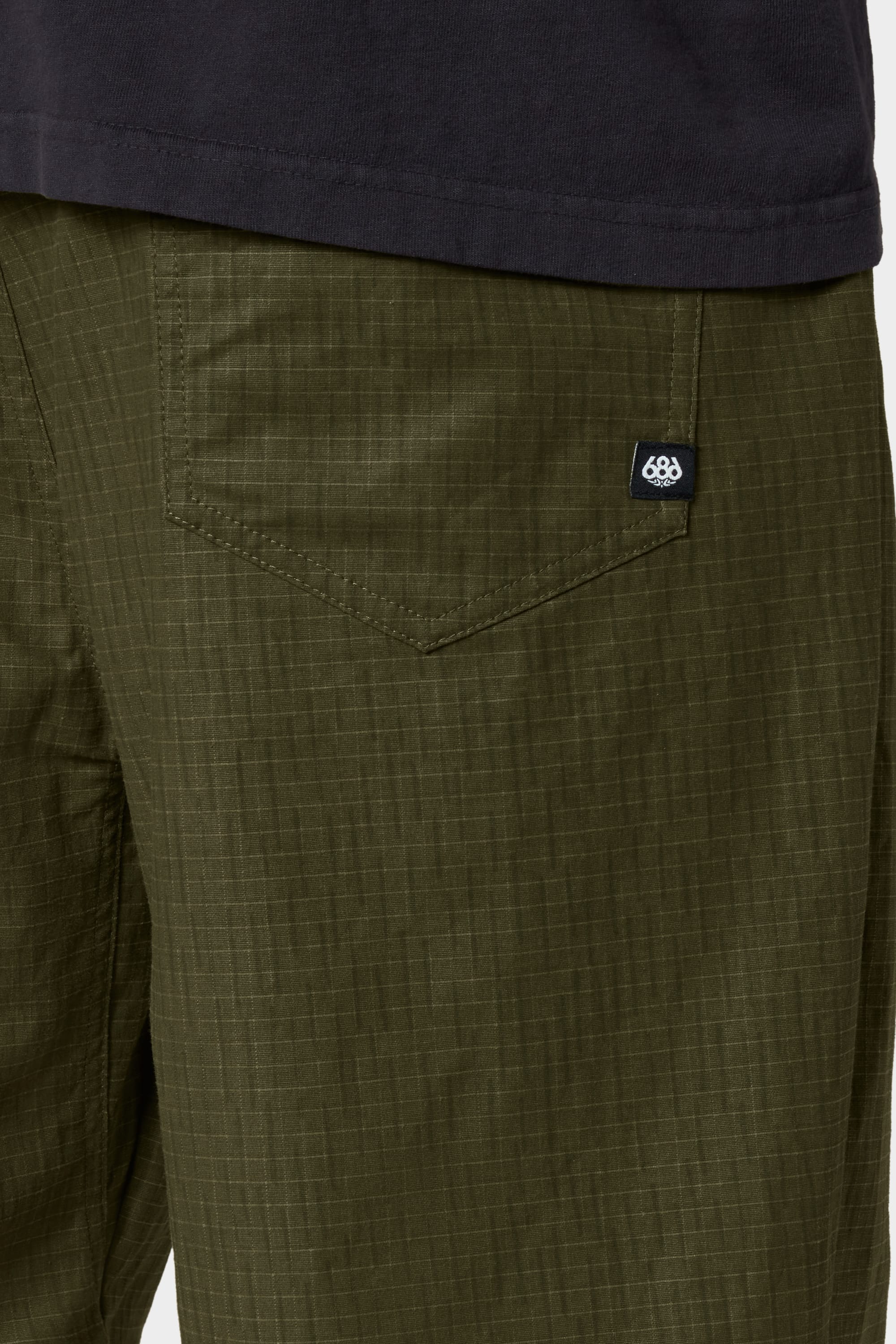 Close-up of a person wearing the 686 Cruiser Pant - Wide Fit in olive green ripstop fabric, featuring a visible back pocket with a small black tag, paired with a dark shirt.