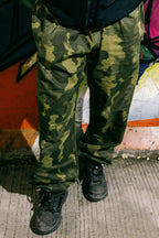 A person wearing 686 Cruiser Pant - Wide Fit by 686 and black shoes stands on a concrete surface in front of a colorful graffiti wall.