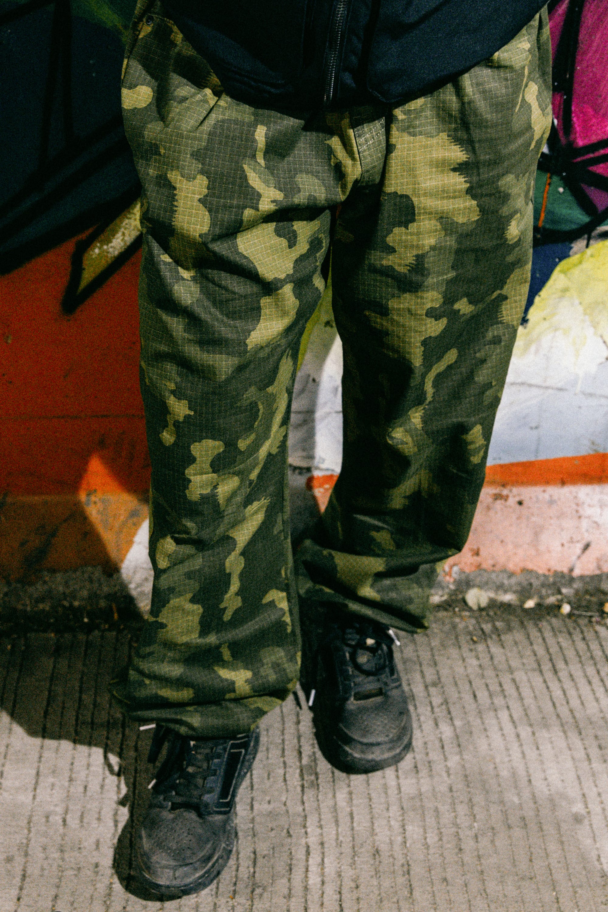 A person wearing 686 Cruiser Pant - Wide Fit by 686 and black shoes stands on a concrete surface in front of a colorful graffiti wall.