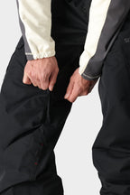 A person wearing the 686 Men's SMARTY® 3-in-1 Cargo Bib unzips a ventilation zipper on the thigh area of the shell bib.