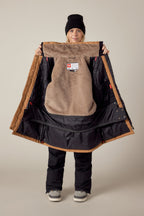 A smiling person in winter clothing and a black beanie holds open the 686 Womens Spirit Insulated Jacket, displaying its soft tan faux-fur lined interior and the 686 brand label.