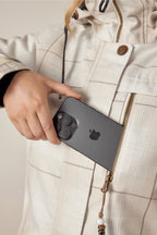 A person wearing the 686 Womens Spirit Insulated Jacket is placing a black smartphone with three camera lenses into the jacket’s zippered chest pocket. Only their hand and upper body are visible.