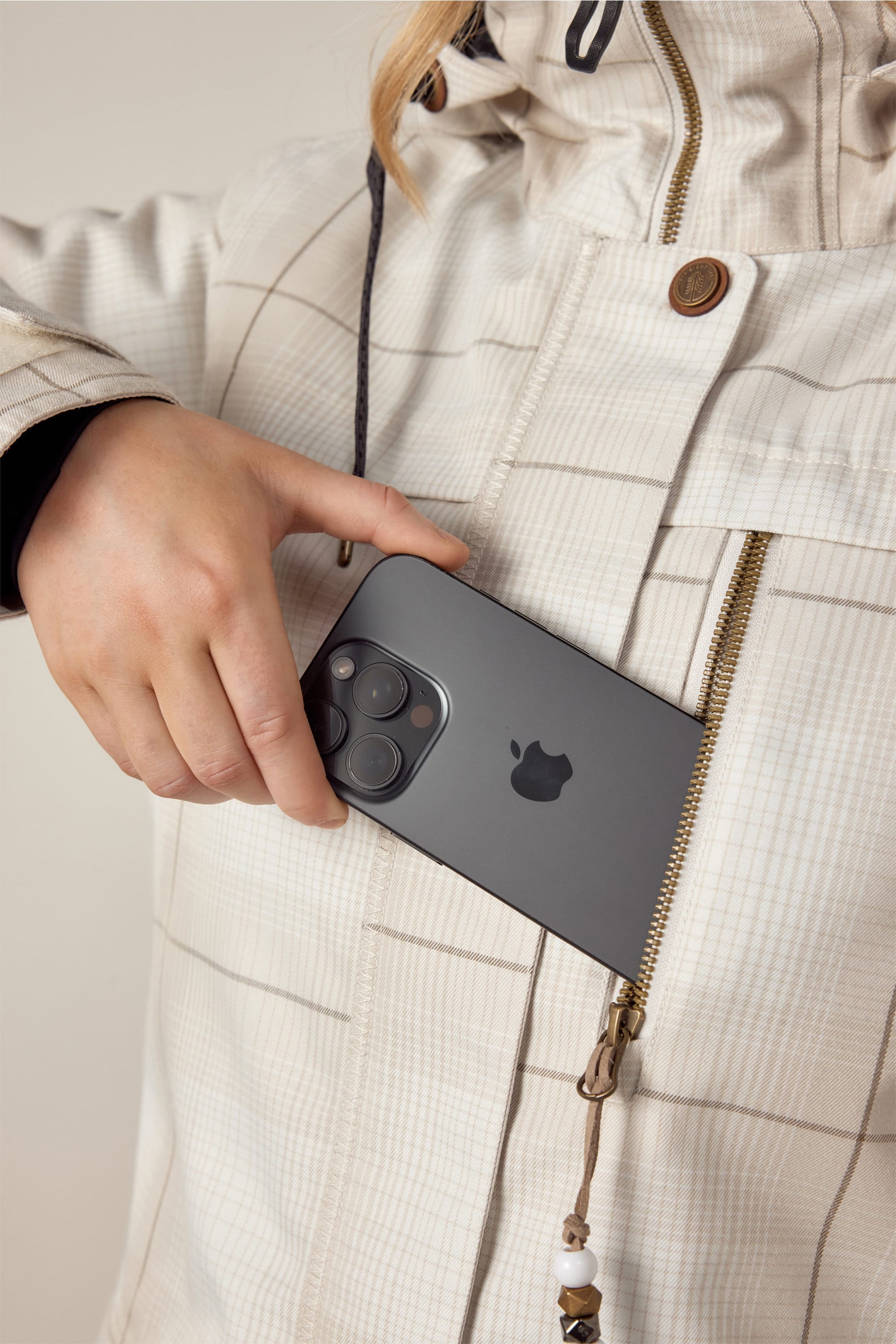 A person wearing the 686 Womens Spirit Insulated Jacket is placing a black smartphone with three camera lenses into the jacket’s zippered chest pocket. Only their hand and upper body are visible.