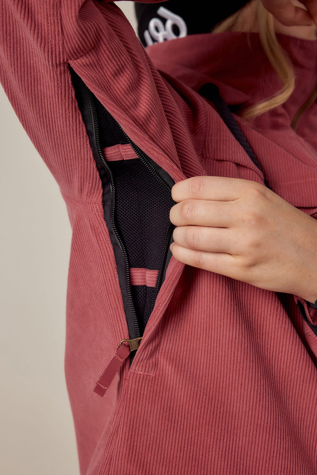 A person wearing the 686 Womens Spirit Insulated Jacket in pink unzips a side vent, revealing black mesh lining and pink straps inside the jacket.