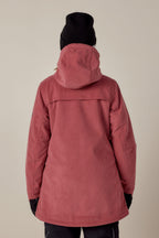 A person is shown from the back against a plain light background, wearing the 686 Womens Spirit Insulated Jacket by 686 in dusty rose with faux-fur lined hood, paired with a black knit beanie, black gloves, and dark pants.