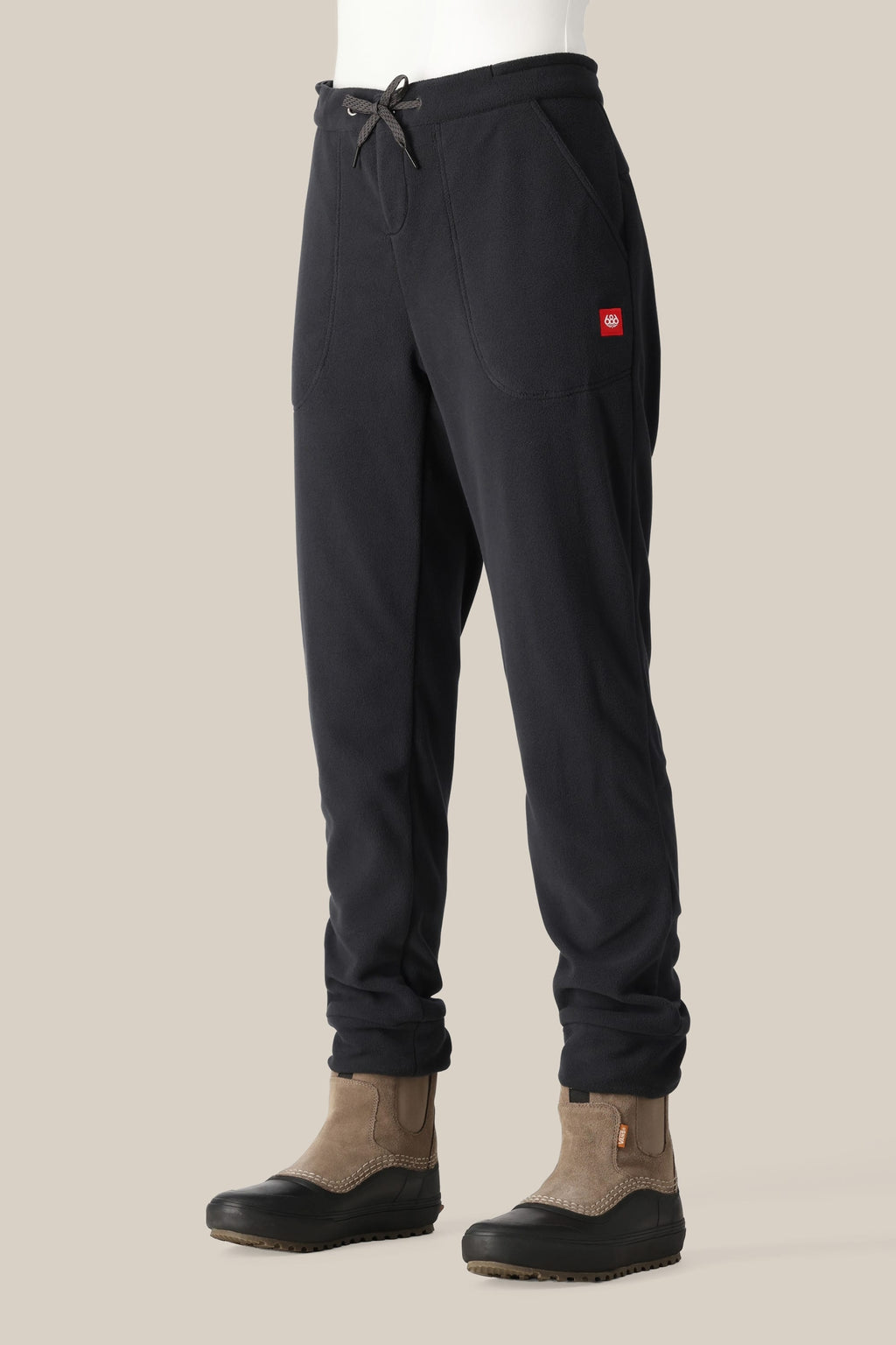 A woman wearing 686 Women's SMARTY® 3-in-1 Cargo Pant by 686 stands against a plain light beige background, pairing the versatile pants with brown slip-on boots.