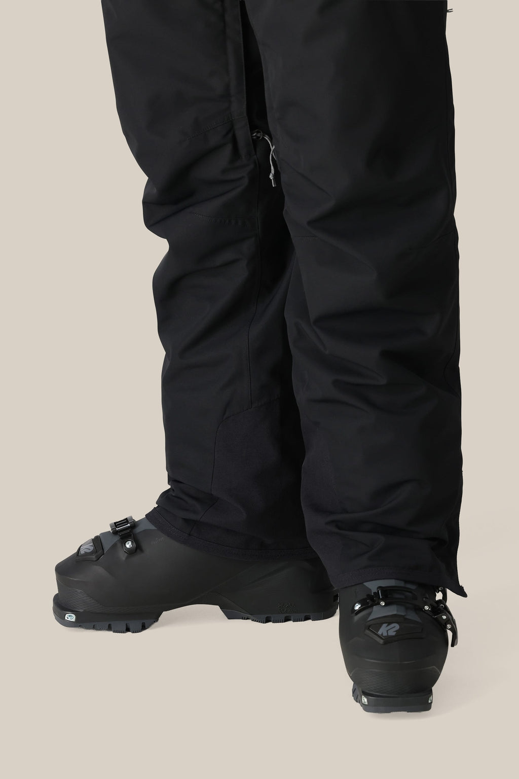 A person wears 686 Women's SMARTY® 3-in-1 Cargo Pants by 686, featuring a removable sweatpant liner, and black ski boots, standing on a light background with only their lower legs and feet shown.
