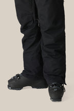 A person wears 686 Women's SMARTY® 3-in-1 Cargo Pants by 686, featuring a removable sweatpant liner, and black ski boots, standing on a light background with only their lower legs and feet shown.