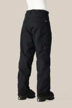 A rear view of a person wearing 686 Women's SMARTY® 3-in-1 Cargo Pant in black with back pockets, thigh zippers, and a removable liner, paired with black snow boots against a plain beige background. Brand: 686.