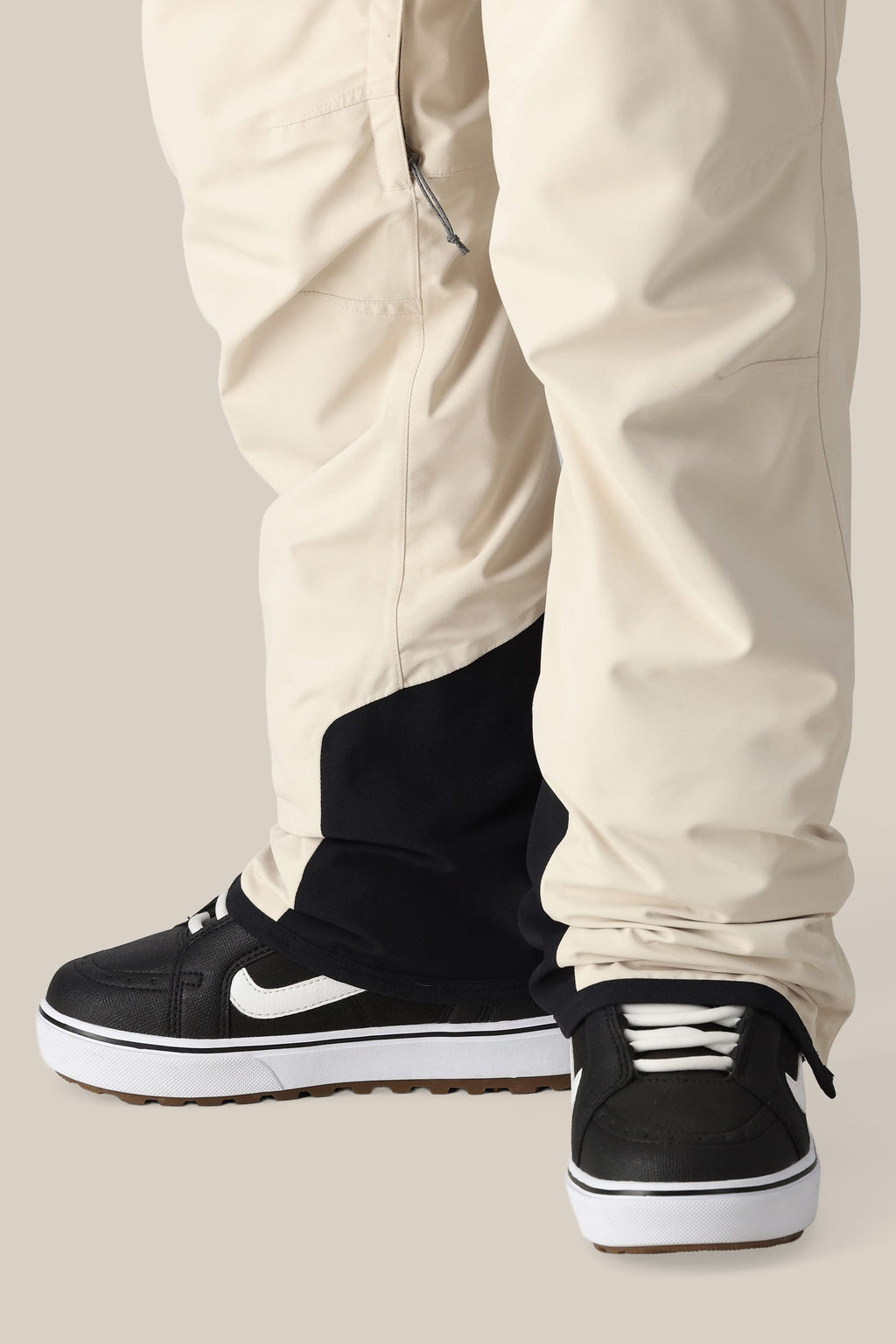 A person wears the 686 Women's SMARTY® 3-in-1 Cargo Pant—baggy, cream-colored cargo pants with a removable sweatpant liner—paired with black and white sneakers. The versatile design lets the pants partially cover the shoe tops.