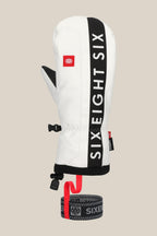 The 686 Mens Team Merino Mitt by 686 features white and black colors, SIX EIGHT SIX printed vertically, internal finger separation for warmth, a red logo patch, and an attached black and red wrist leash. Displayed on a beige background.
