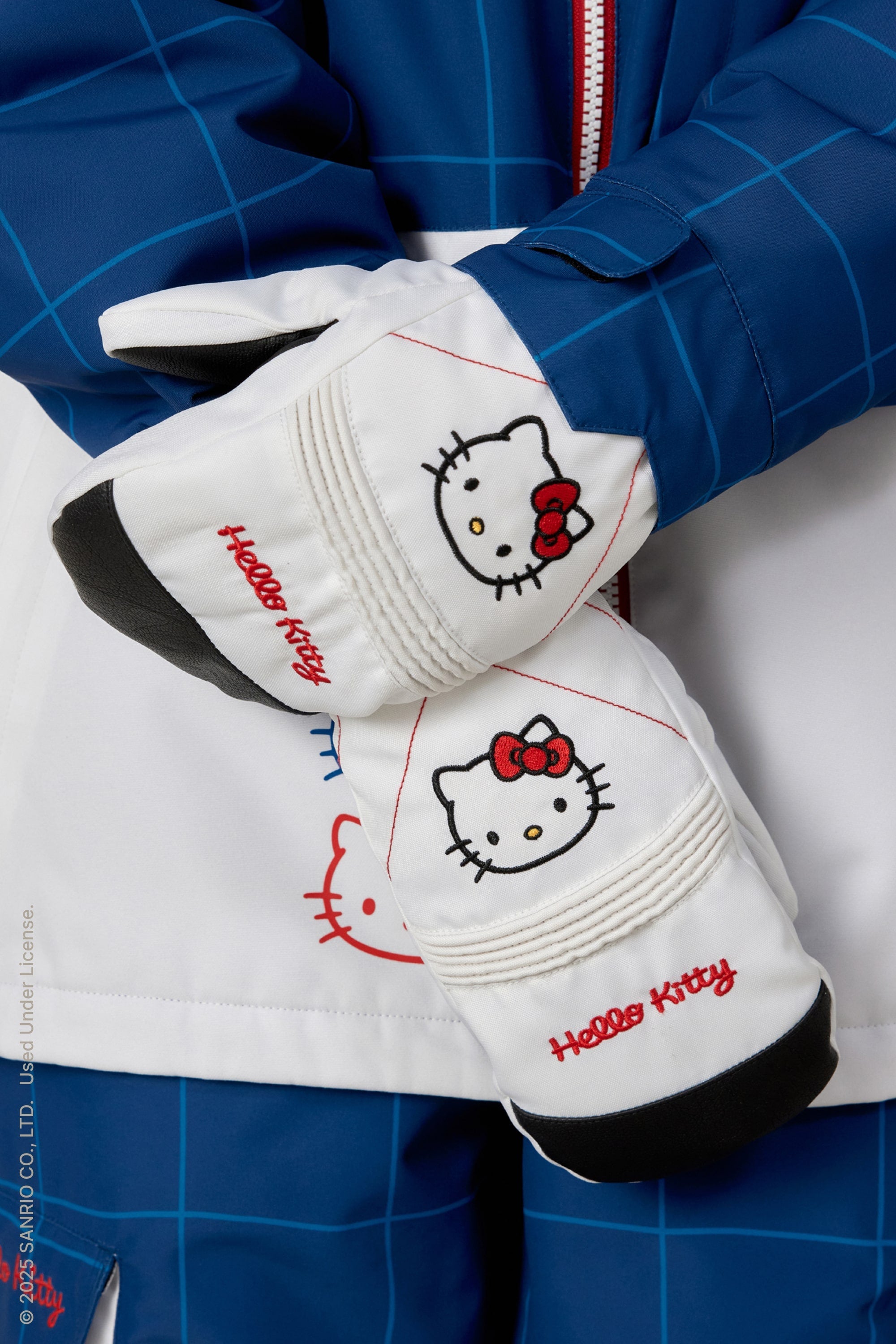 A person in blue and white winterwear shows their 686 Women's Jubilee™ Mitts by 686, featuring Hello Kitty’s face and red embroidery, with light insulation for added warmth.