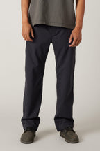A person stands facing forward against a plain light background, wearing a grey t-shirt, grey shoes, and 686 Men's Unwork® Pant - Relaxed Loose Fit in dark navy by 686. The image is cropped at the shoulders.