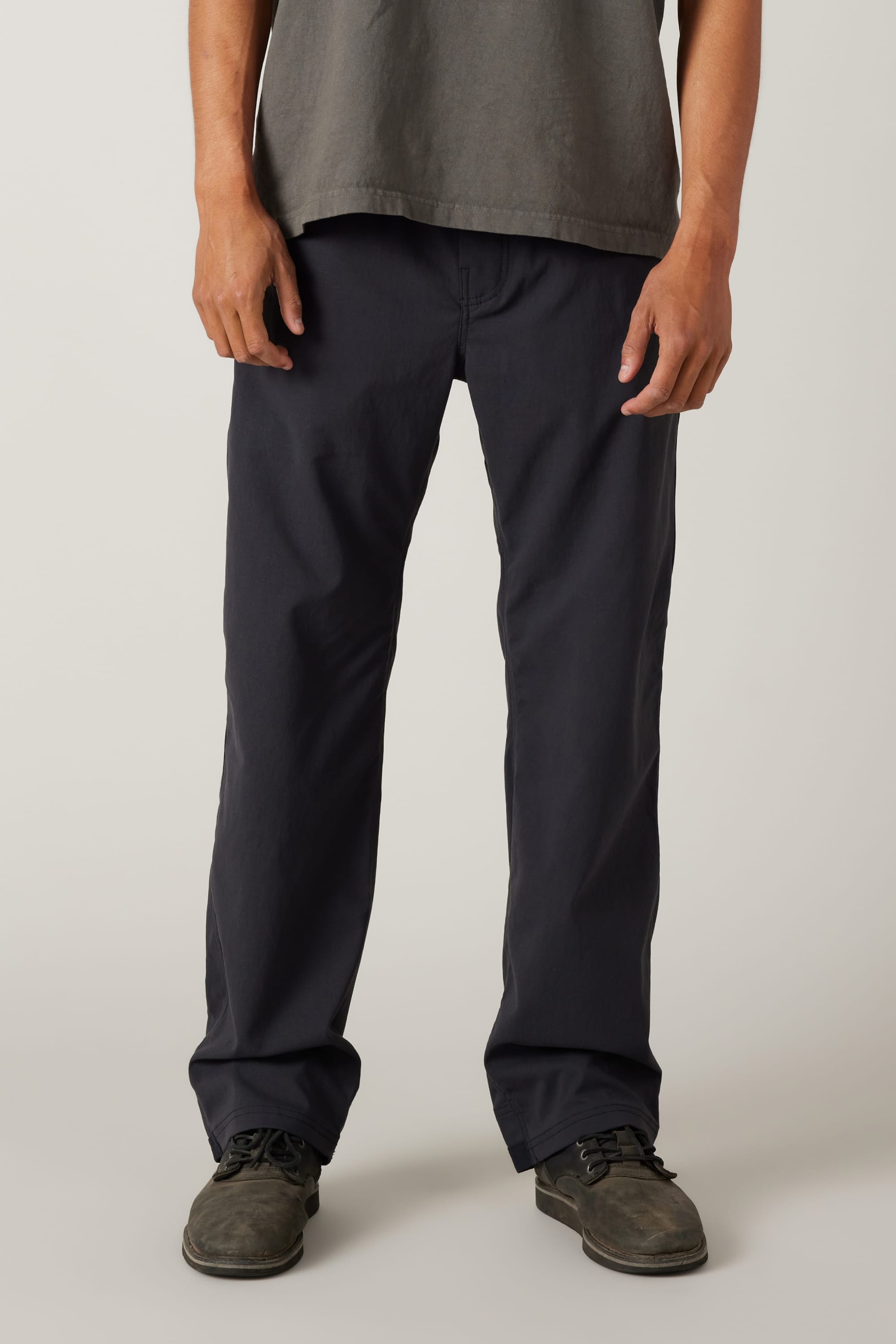 A person stands facing forward against a plain light background, wearing a grey t-shirt, grey shoes, and 686 Men's Unwork® Pant - Relaxed Loose Fit in dark navy by 686. The image is cropped at the shoulders.