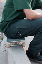 Wearing the 686 Men's Unwork® Pant - Relaxed Loose Fit, a person sits on a skateboard atop a concrete ledge outdoors. Their face is not visible in the image.