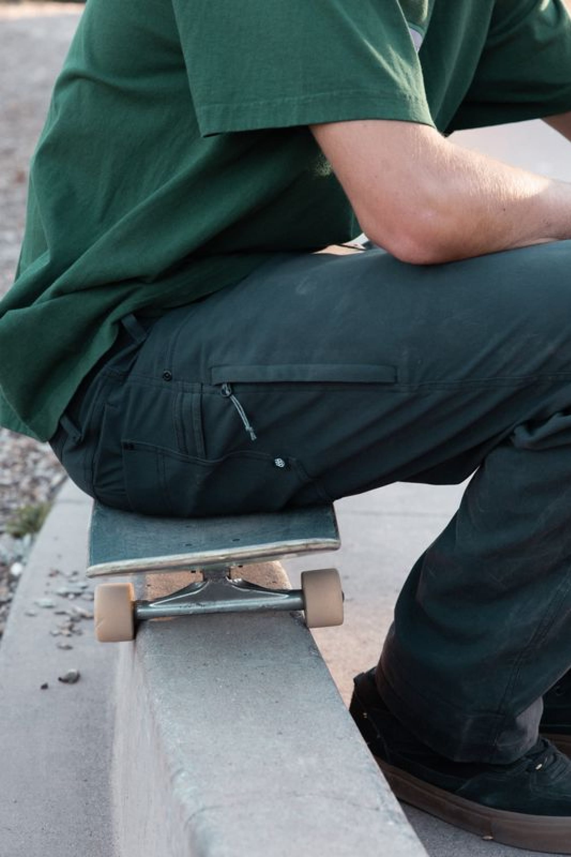 Wearing the 686 Men's Unwork® Pant - Relaxed Loose Fit, a person sits on a skateboard atop a concrete ledge outdoors. Their face is not visible in the image.