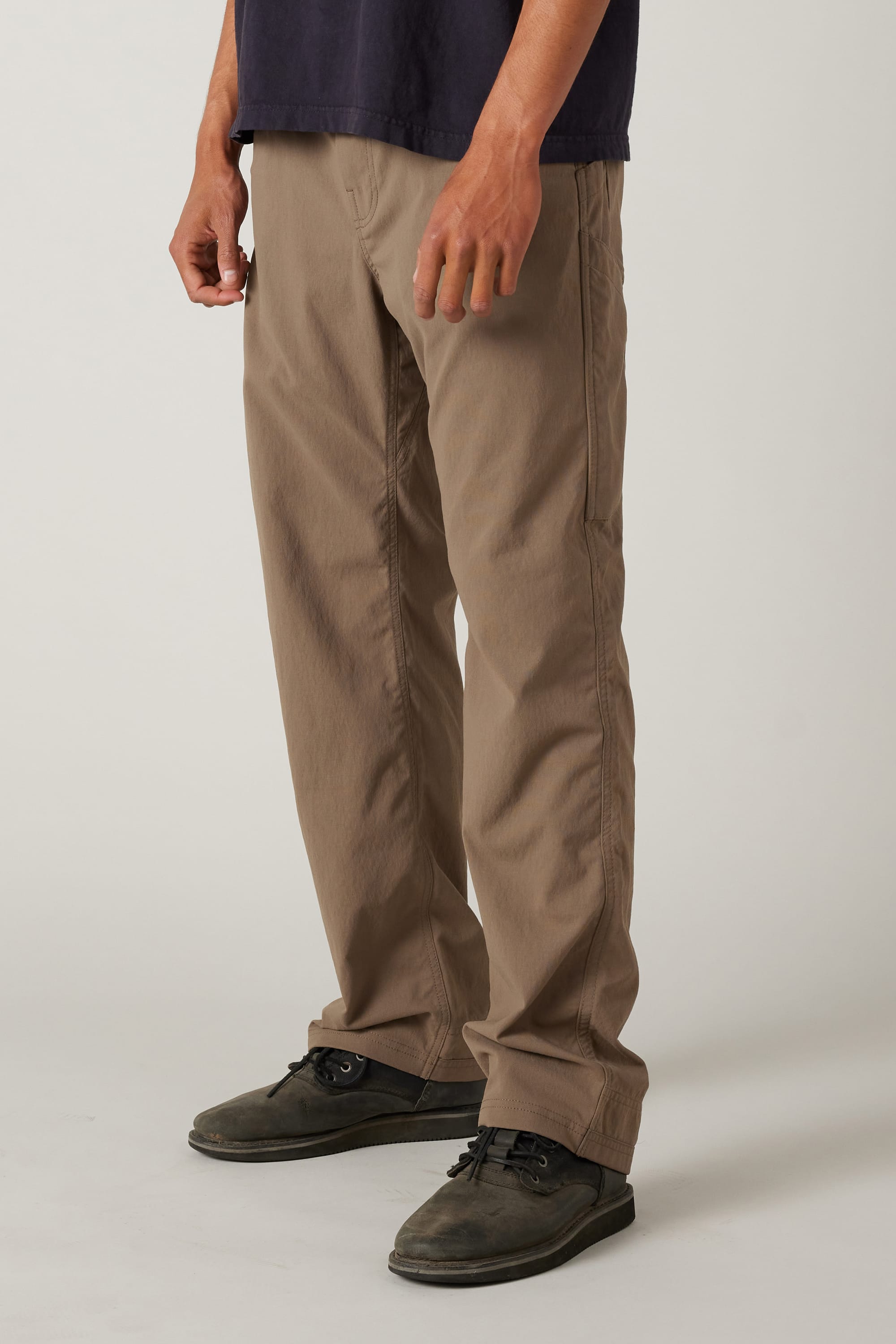 A person models the 686 Men's Unwork® Pant - Relaxed Loose Fit by 686, showing only the lower half of their body. The durable khaki pants are styled with a dark shirt and shoes, against a plain light background.