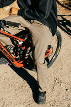 A person in the 686 Men's Unwork® Pant - Relaxed Loose Fit by 686 sits on a red mountain bike along a dirt path, sunlight casting shadows on the ground.