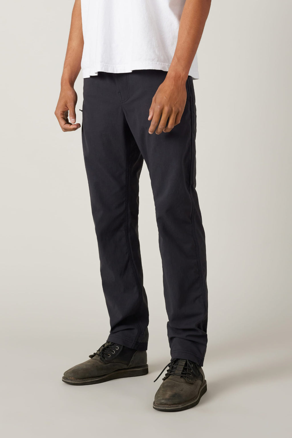 A person stands against a plain light background, wearing a white short-sleeve shirt, 686 Men's Unwork® Pant - Slim Fit in dark navy, and dark gray lace-up shoes, with their arms relaxed at their sides.