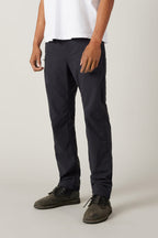 A person stands against a plain light background, wearing a white short-sleeve shirt, 686 Men's Unwork® Pant - Slim Fit in dark navy, and dark gray lace-up shoes, with their arms relaxed at their sides.