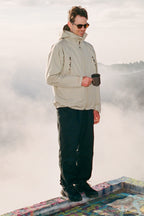 A man stands outdoors on a colorful surface, holding a mug, in thick fog that hides distant hills. He wears sunglasses, a light jacket, and the 686 Men's Everywhere® Pant - Wide Fit by 686 in stain-resistant black.