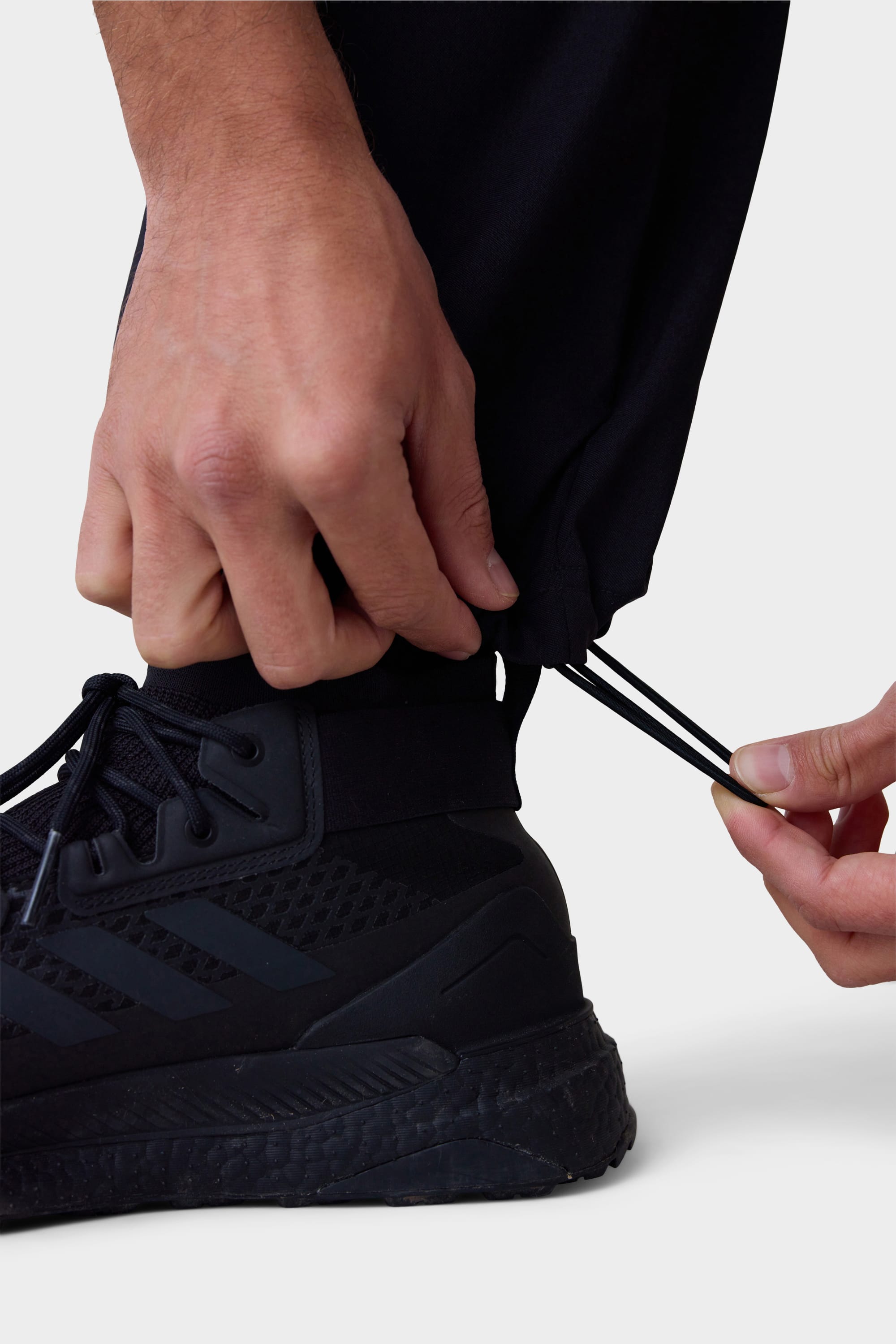 A person adjusts the ankle drawstring on 686 Men's Everywhere® Pant - Wide Fit by 686, styled with black athletic shoes.