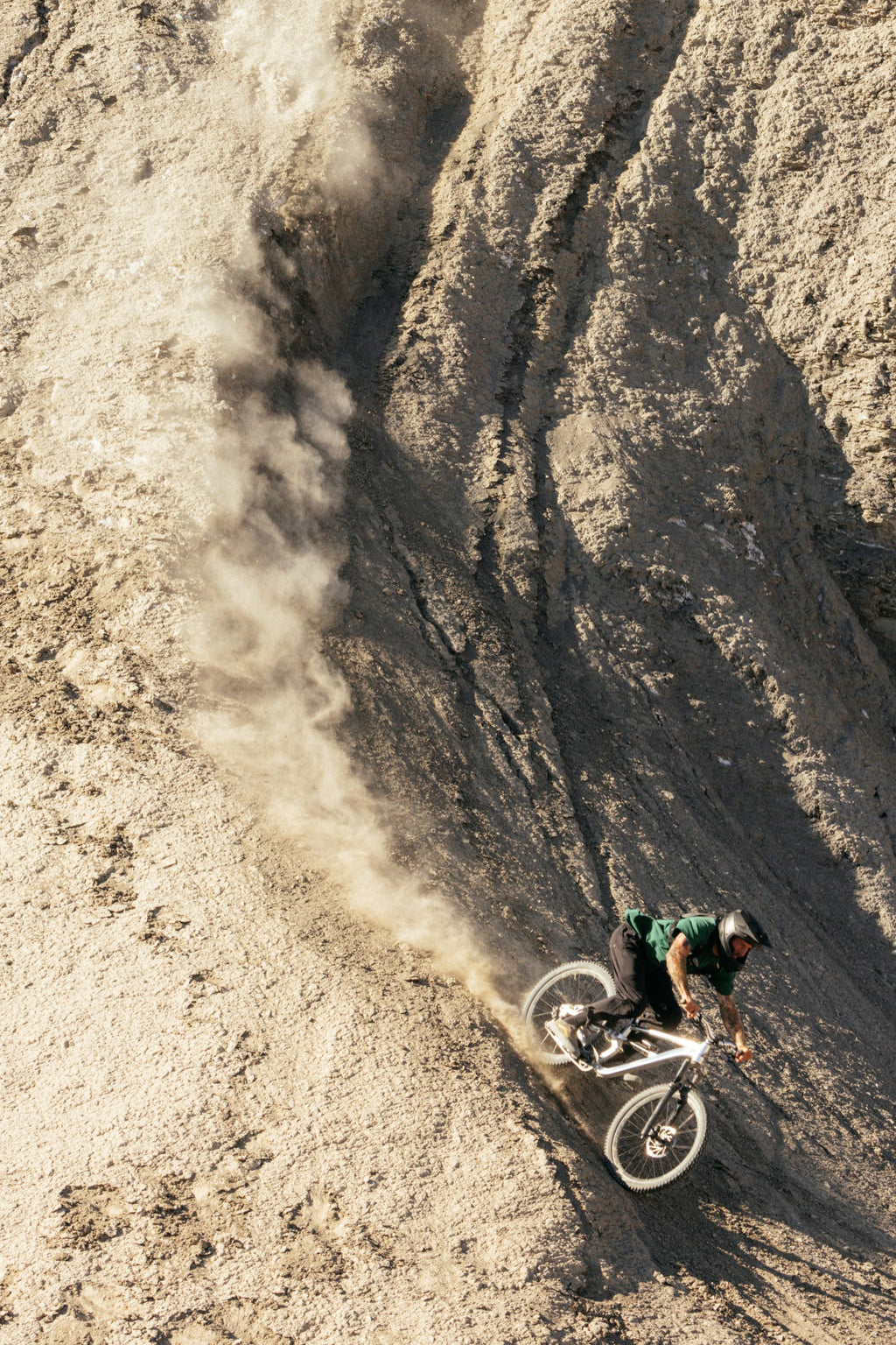 Wearing 686 Men's Everywhere® Pant - Wide Fit, a mountain biker in a helmet and dark clothing rides confidently down a steep, rocky slope, dust rising as sunlight highlights the rugged terrain.