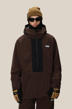 A person wearing the 686 Men's Ghost™ 2.5L Anorak—a rugged brown nylon hooded jacket with black accents—plus matching pants, tan gloves, a tan beanie, and black sunglasses stands against a plain beige background in a modern shorter fit.