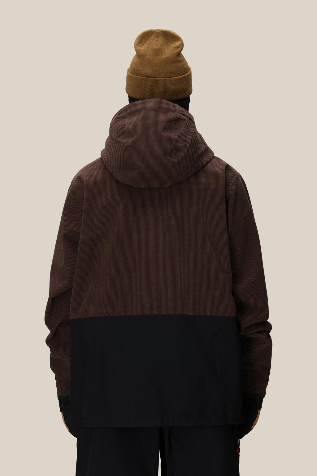A person in a brown beanie, black pants, and the 686 Men's Ghost™ 2.5L Anorak stands with their back to the camera against a plain beige background.