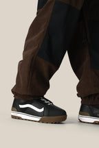 Someone wearing the 686 Ghost™ 2.5L Pant and black sneakers with white detailing and a brown sole stands on a neutral beige background.