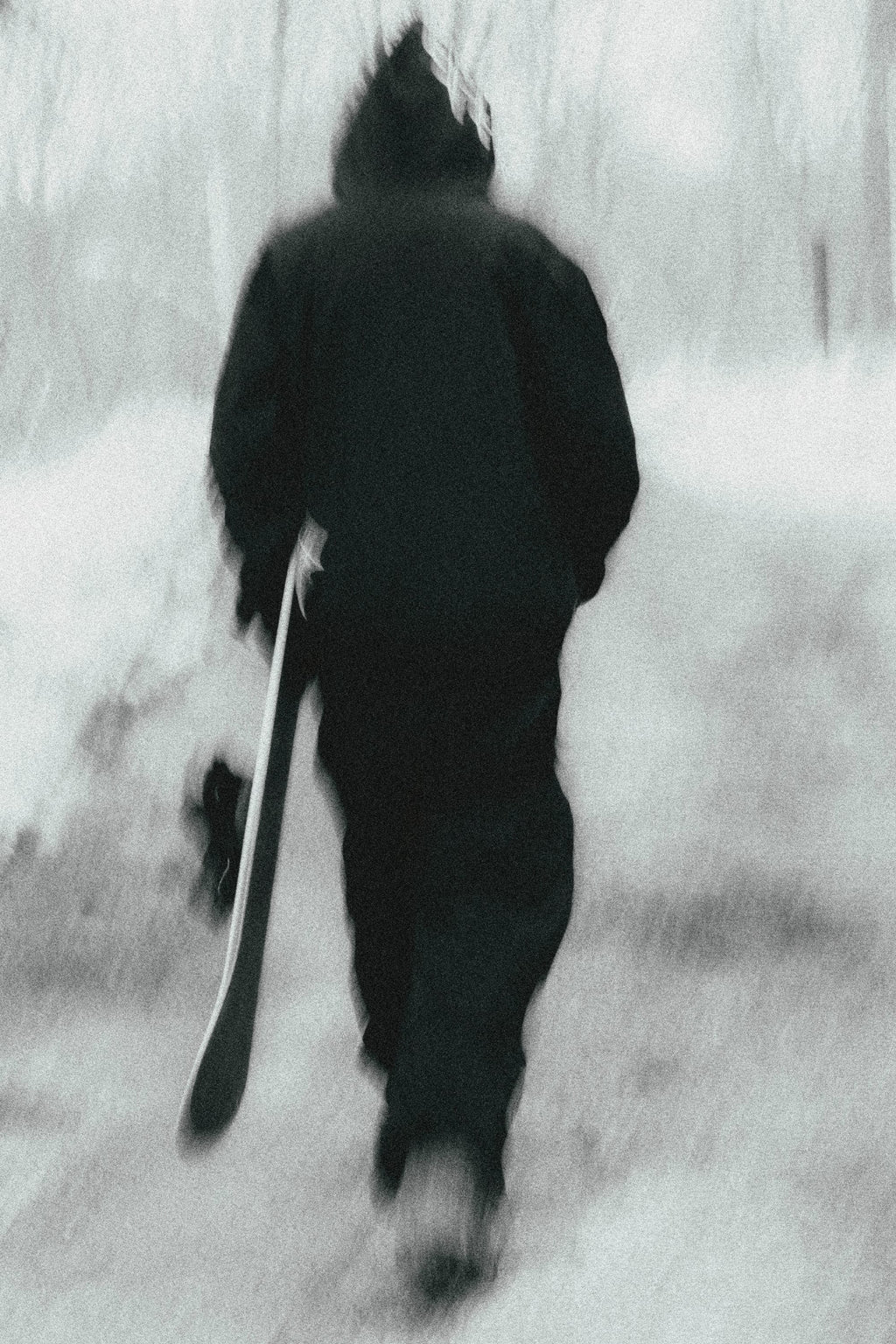 Wearing the 686 Ghost™ 2.5L Pant by 686, a person in dark winter clothes strolls down a snowy path with a snowboard in hand. The blurred image adds a dreamy, ethereal vibe to the scene.