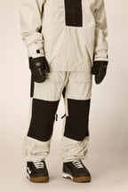 A person is wearing the 686 Ghost™ 2.5L Pant by 686 with a matching checkered beige and black snow jacket, black gloves, and black-and-white snow boots, standing against a plain background.