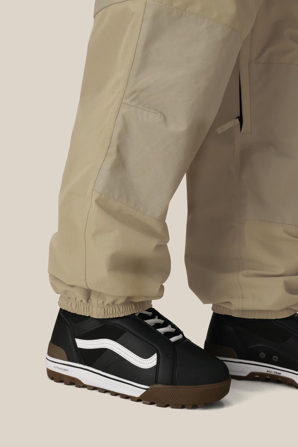 A person wears 686 Ghost™ 2.5L Pants and black sneakers with white stripes and brown soles, standing against a plain light background.