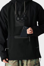 A person in the 686 Mens Waterproof Hoody, fleece-lined for comfort, with the 686 logo and front zippered pocket, pairs it with camo pants while placing a smartphone into the hoody’s pocket.