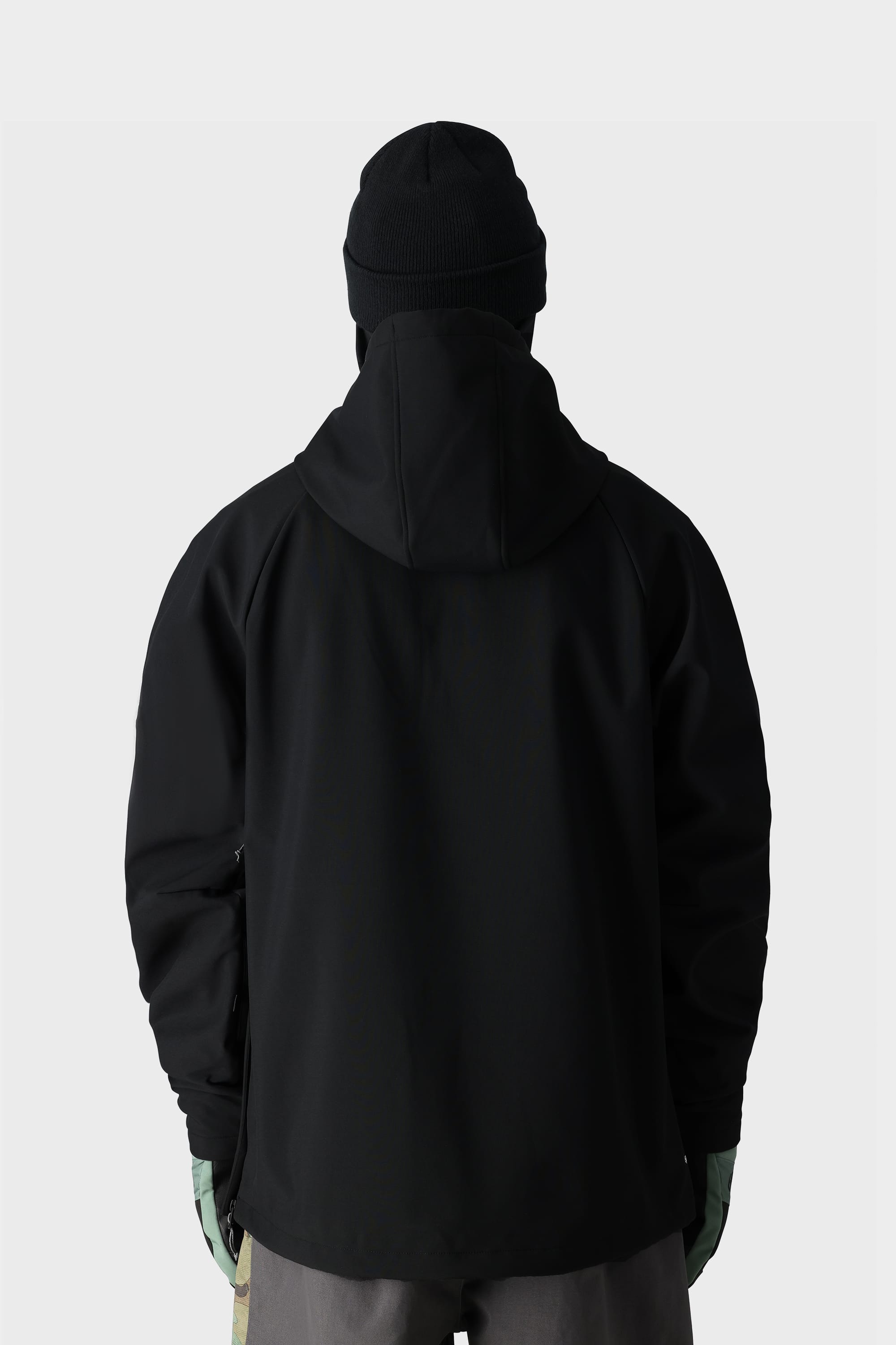 A person is seen from behind, standing against a plain light background, wearing the 686 Mens Waterproof Hoody in black by 686, along with green gloves and gray pants.