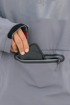 A person’s hand slips a smartphone into the front zippered pocket of the gray 686 Men’s Waterproof Hoody, featuring a soft fleece lining.