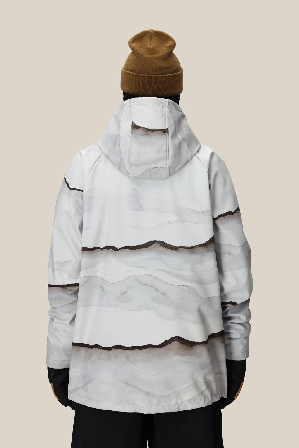A person wearing the 686 Mens Waterproof Hoody by 686, featuring a fleece lining and white fabric with abstract gray and brown wave patterns, along with a brown beanie and black gloves, stands with their back to the camera against a beige background.